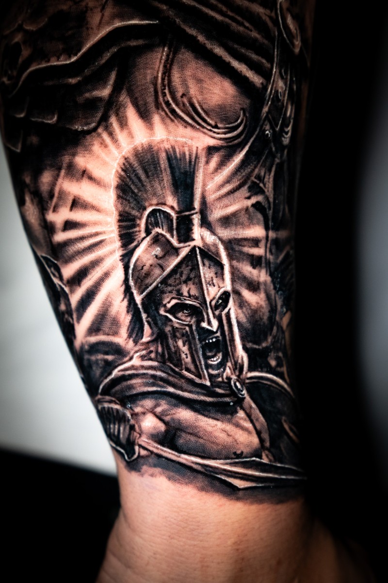 Close-up of an armored warrior tattoo, showing the eye, helmet, light rays and shading.