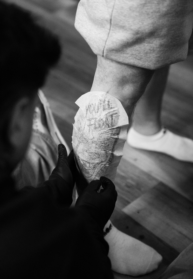 Gloved hands placing tattoo transfer paper around a client's calf.