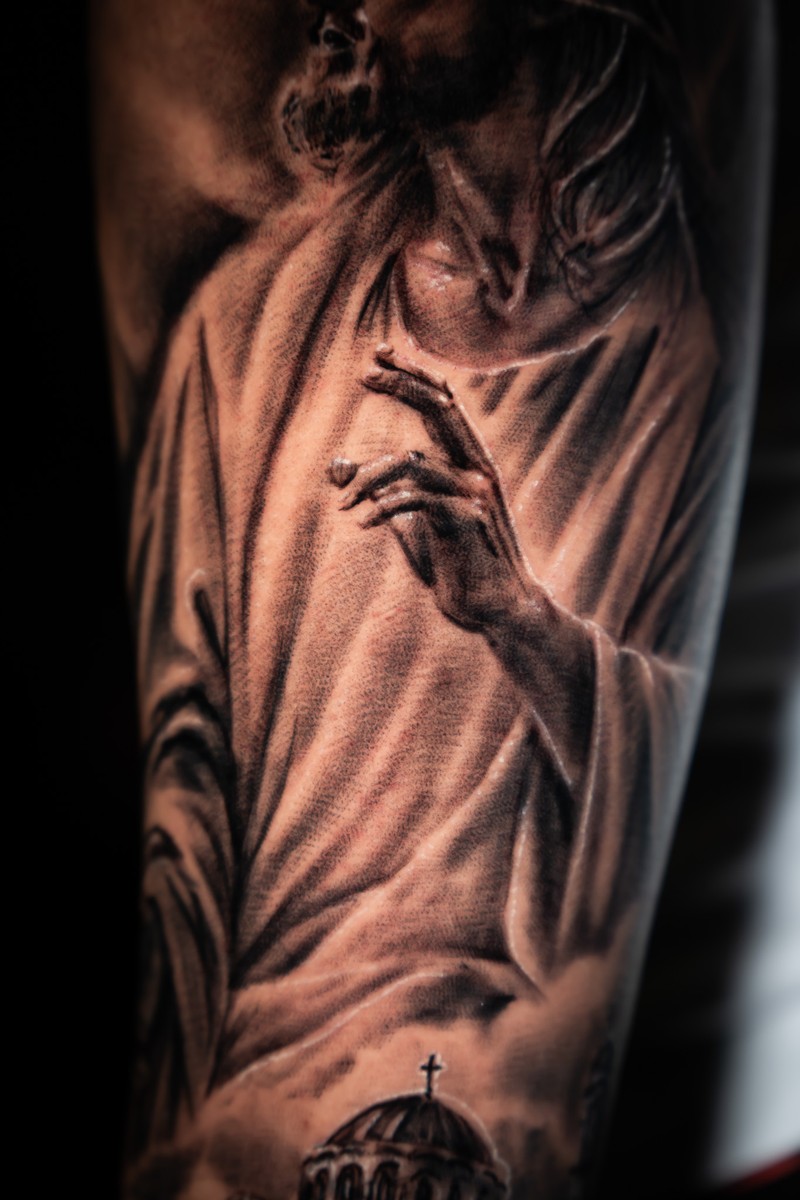 Detail of the same Jesus tattoo, showing the hand, robes and church architecture.